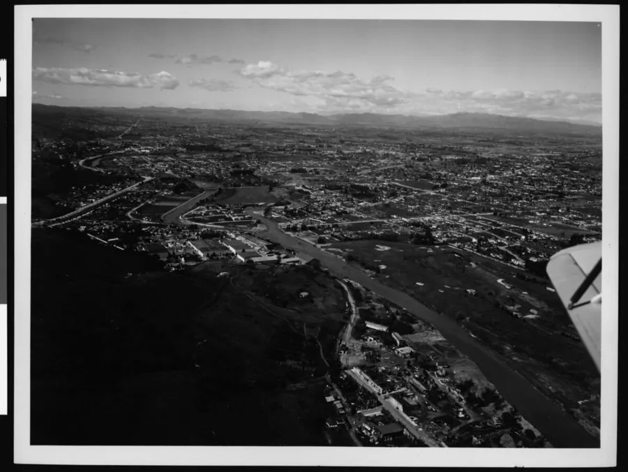 Black-and-white aerial photo of the flooded Los Angeles River at the Lankershim Boulevard bridge in 1938, with the plane's wingtip in the foreground and the city and mountains beyond.
